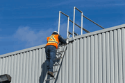 Technician in a safety vest climb a ladder to perform safety inspection services, including rigorous inspection testing services on rooftop guardrails