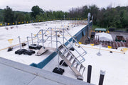 Non-penetrating, modular aluminum roof-crossover-bridge providing safe, non-slip access over pipes and level changes on a commercial flat roof