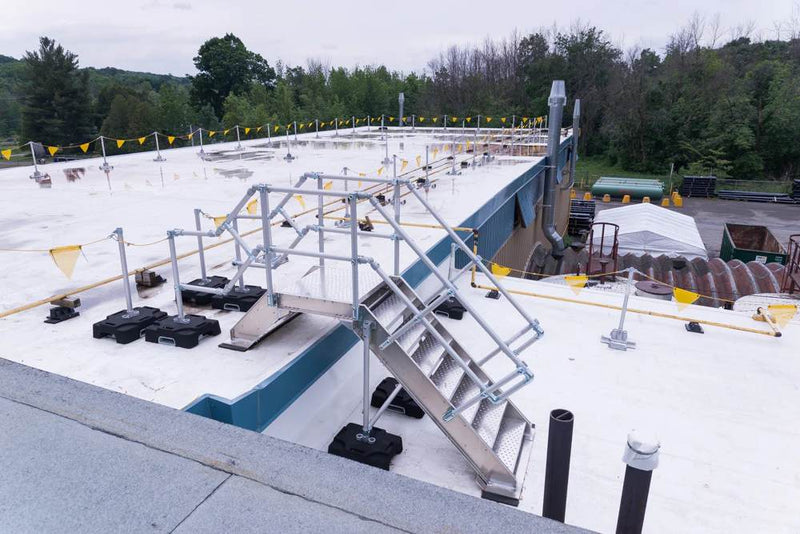 Non-penetrating, modular aluminum roof-crossover-bridge providing safe, non-slip access over pipes and level changes on a commercial flat roof